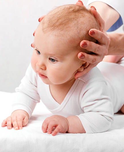 Six month baby girl receiving osteopathic or chiropractic treatment in pediatric clinic. Manual therapist manipulates chils's head and neck