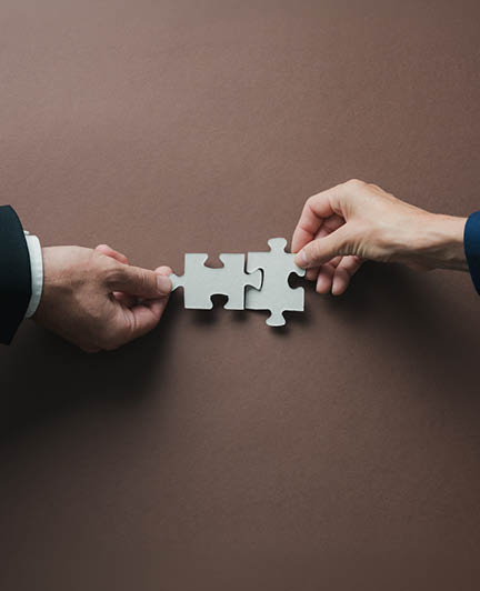 Teamwork and partnership conceptual image - hands of a businessman and businesswoman joining blank matching puzzle pieces over brown background.